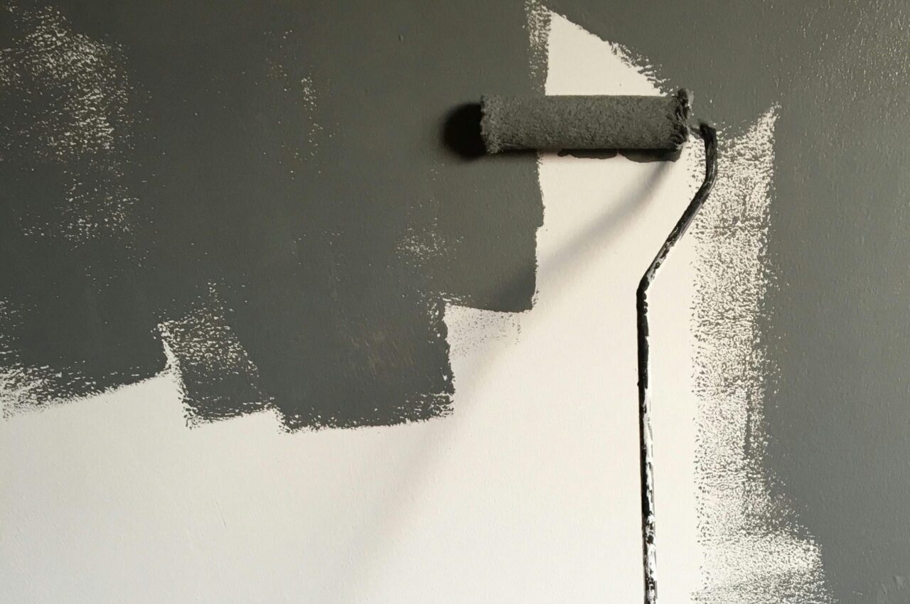A hand painting a wall gray with a roller during a house renovation project.